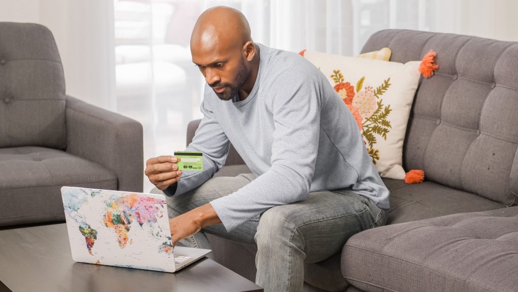 Bald man uses a credit card for online shopping at home on a couch.
